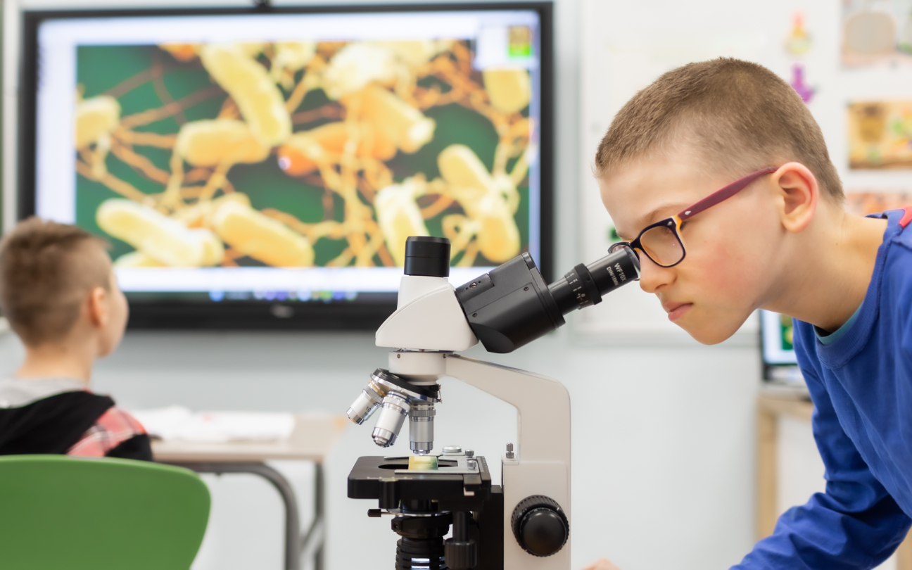 Chłopiec patrzący w mikroskop podczas zajęć z biologii